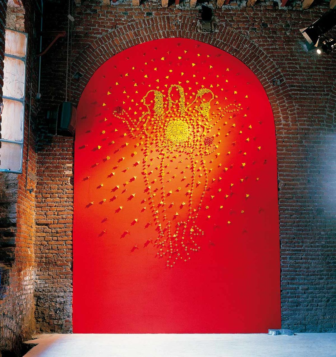 The sun 1998, Installation made by Kazumasa Mizokami, the three goddesses are outlined with small yellow flowers on a bright red arched panel.   the other yellow flowers spread making the shape of a circle around the goddesses