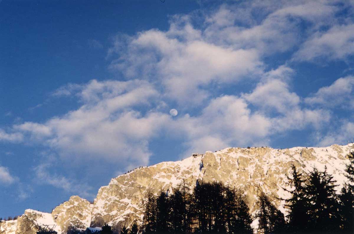 The landscape of Valle d'Ampezzo, title la-Luna-di-giorno, Photo taken by Kazumasa Mizokami On a clear day a white round moon can be seen between the clouds above a snowy mountain.