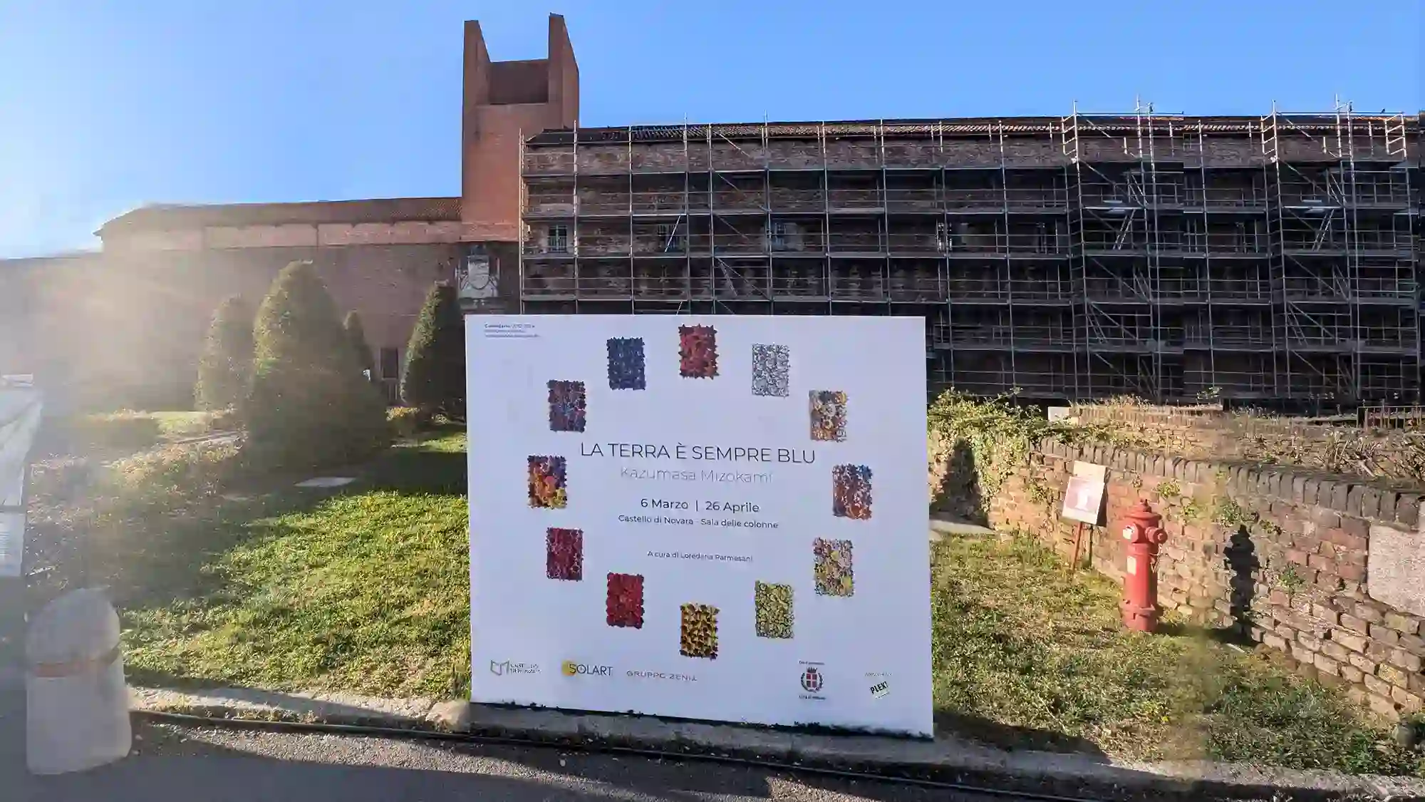A landscape photo seen from the front of Novara Castle. On the lawn is the poster for Kazumasa Mizokami's solo exhibition, titled "The Earth Is Always Blue." From March 6th to April 26th 2026.