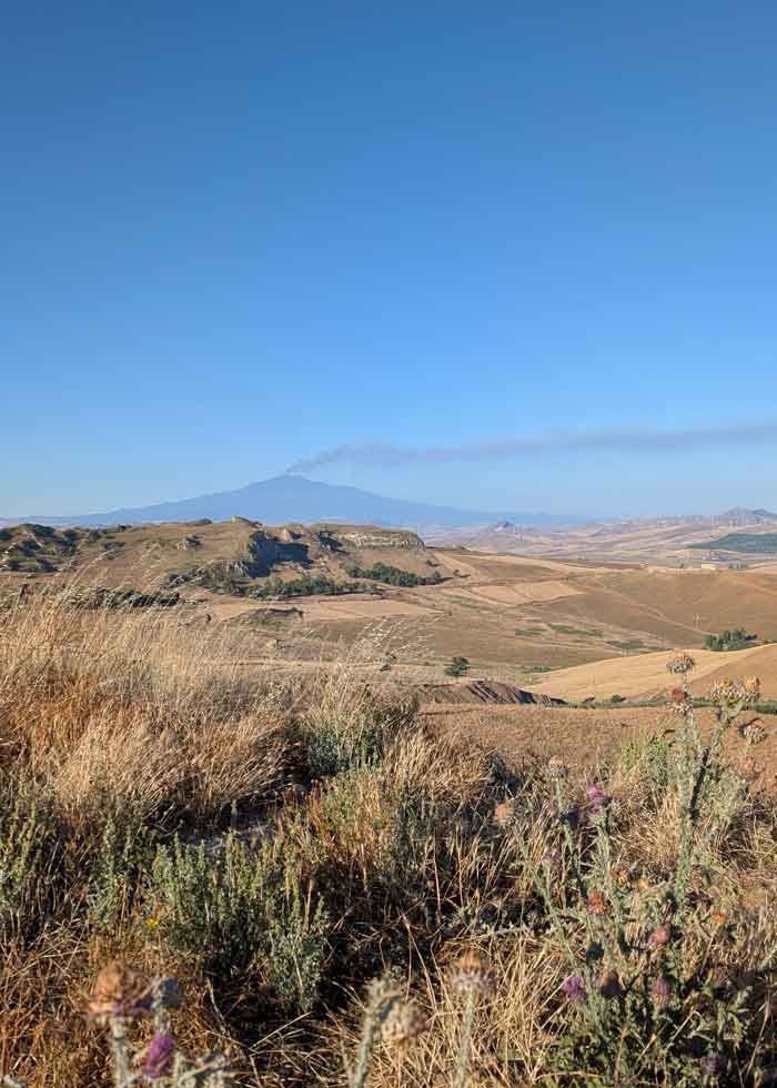 Typical Sicilian countryside landscape. In the background you can see Etna erupting with smoke in the distance.