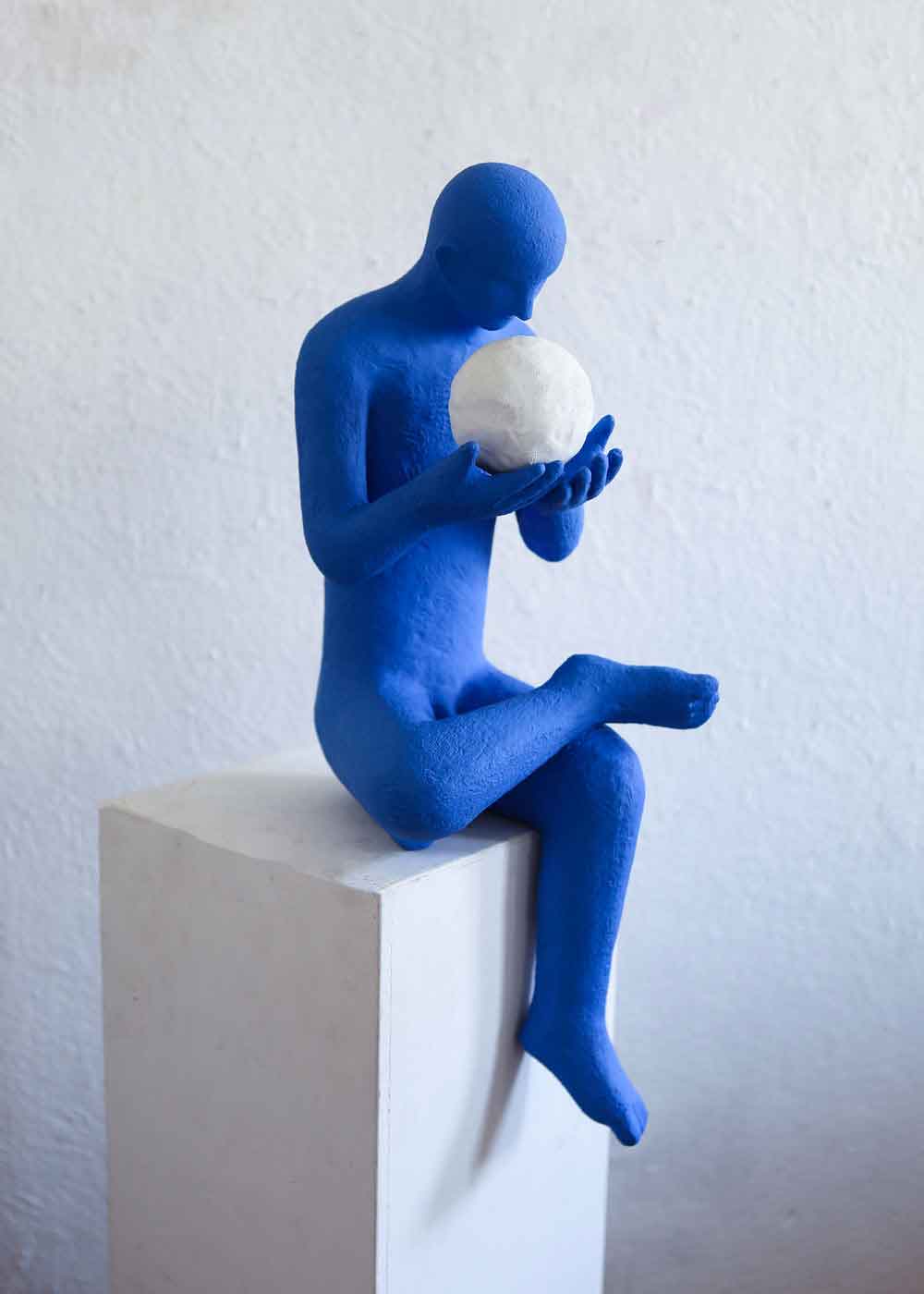 A work from May 2026 by Kazumasa Mizokami, depicting a seated male figure painted blue with a white sphere resting in his hands—appearing as though he is conversing with it.
