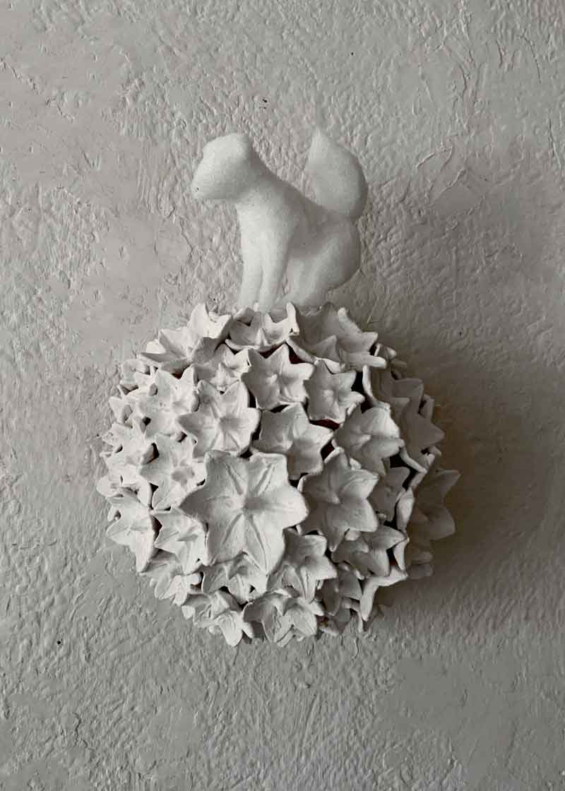 A white squirrel made of lightweight material sits atop a terracotta sphere covered in many small white flowers. A work by Kazumasa Mizokami from July 2026